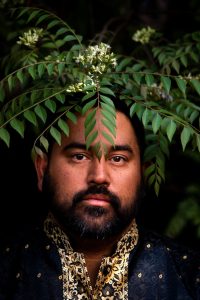 'Tya Tya Sadakal Gujarat I', Portrait of my brother, Asa Jogi, under the curry leaf tree in garden in Harare, Zimbabwe. Known as a 'limdi' tree in Gujarati its presence often indicates that an Indian family is in resid with the duration of their stay represented by the size of the tree, 2022.